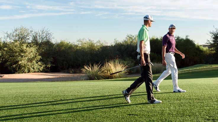 Two male golfers walking and talking on a golf course.