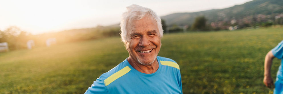 An older man smiles for the camera in a field at sunset during his intramural soccer game.