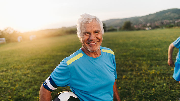 A happy and healthy senior male playing soccer and a sunny field.