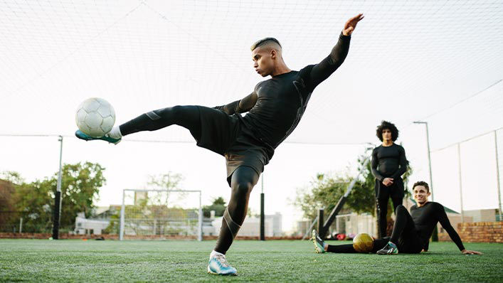 A young soccer player performing a technical kick while his two teammates look on with awe.