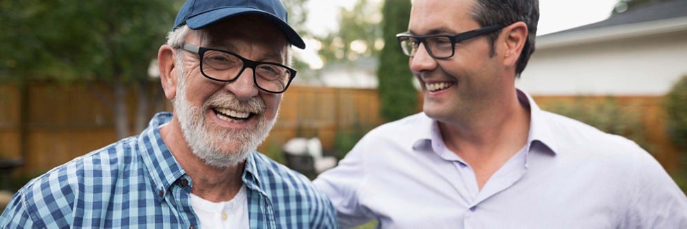 A man and his elderly father laugh together in a backyard.