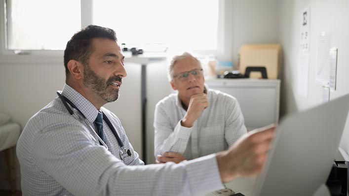 A doctor points to a screen as he explains a procedure to a patient.