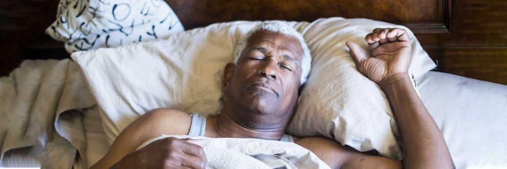 An older man sleeps comfortably in a plush bed. 