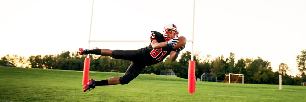 A football player leaps sideways to catch the ball in the end zone.