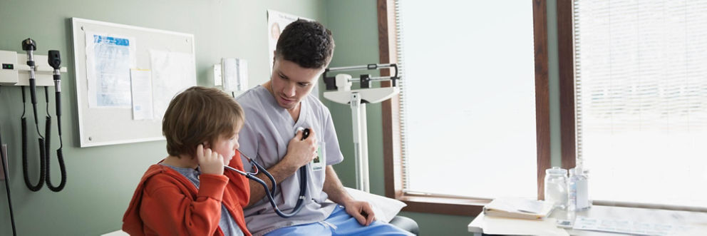 A doctor lets a young patient listen to his heart through a stethoscope.