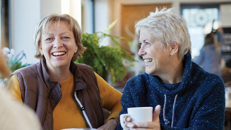 A group of older women enjoy a cup of coffee in a café with friends.