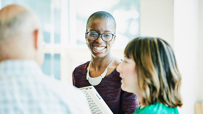 A young woman is smiling at another young woman who is speaking to a small group while holding a dental file.