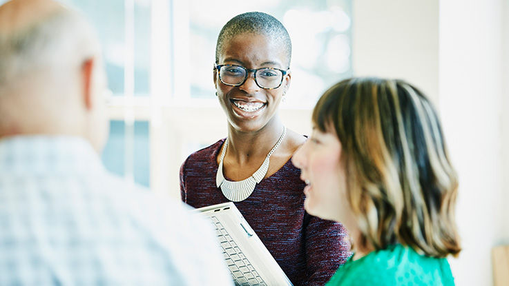 A young woman is smiling at another young woman who is speaking to a small group while holding a dental file.