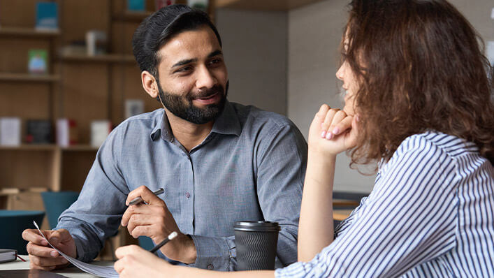 Two colleagues dressed in business attire smile as they discuss a project together