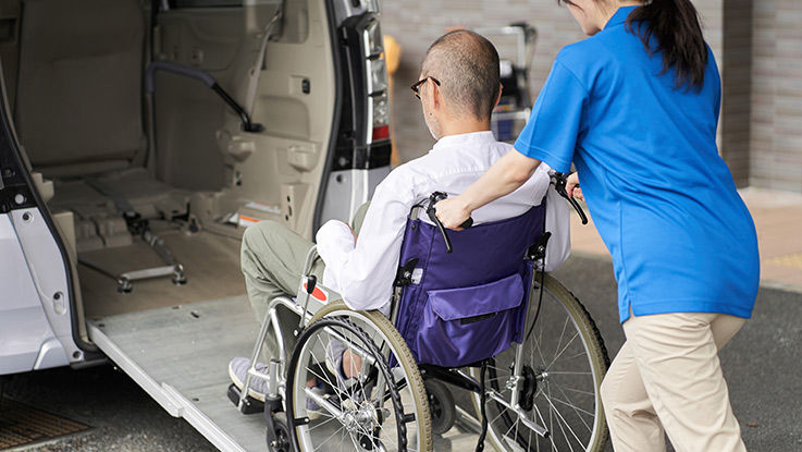 A man in a wheelchair is helped into an accessible van by a medical transport technician.