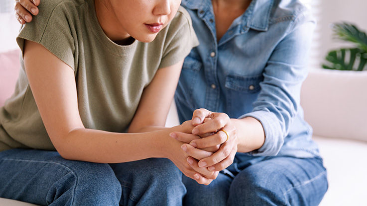 A teenager and parent clasp hands while sitting close together.