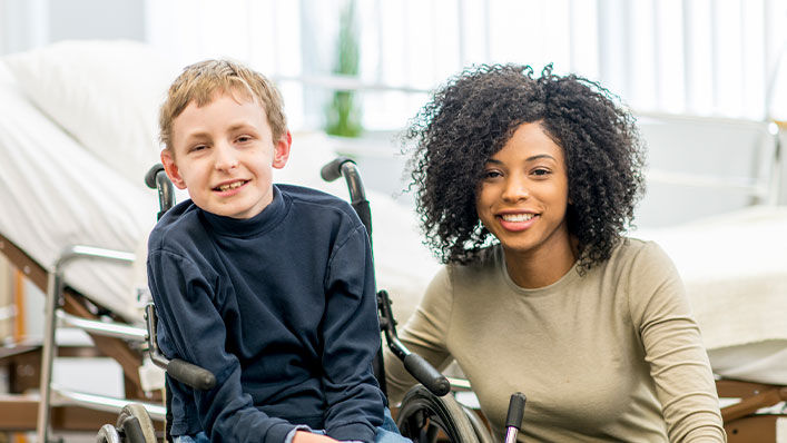 Friendly hospital volunteer poses with a smiling boy in a wheelchair.