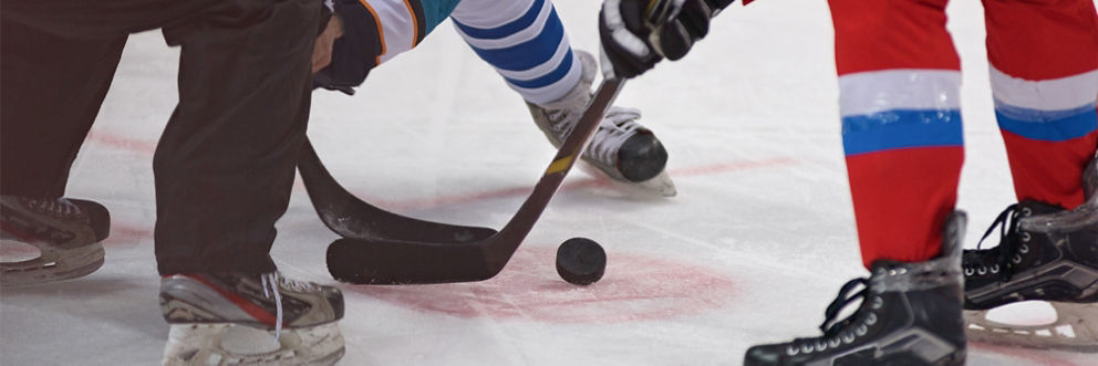 Two hockey players face off over a puck, with a referee standing nearby.