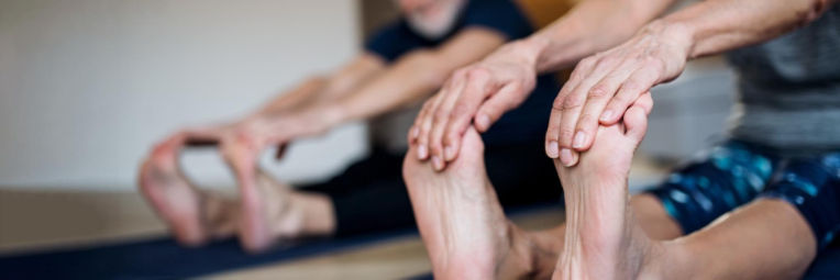 An older man and woman touch their toes in a seated position during a yoga class.