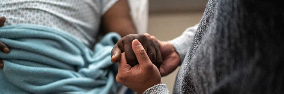 A patient holds their loved one's hand during a hospital visit.