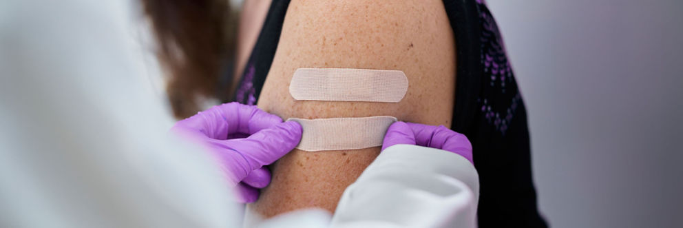 A doctor places a Band-Aid on the arm of a patient who just received a vaccination shot.