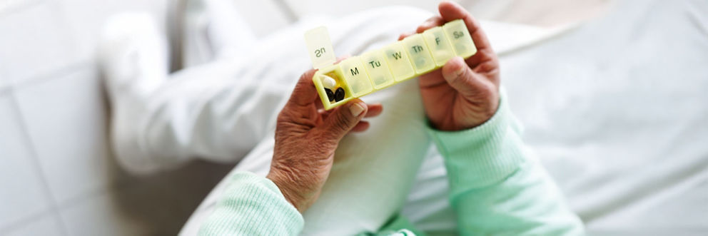 Person sitting and holding a weekly pill container, with Sunday flipped open and several pills inside.