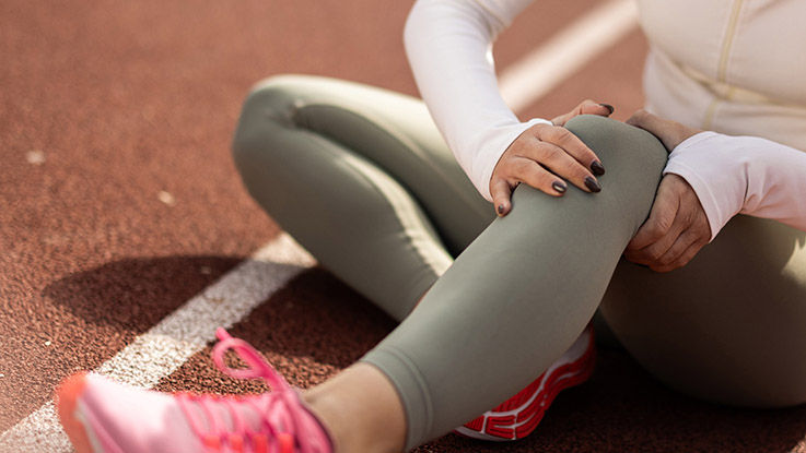 A woman holding her knee on a running track.