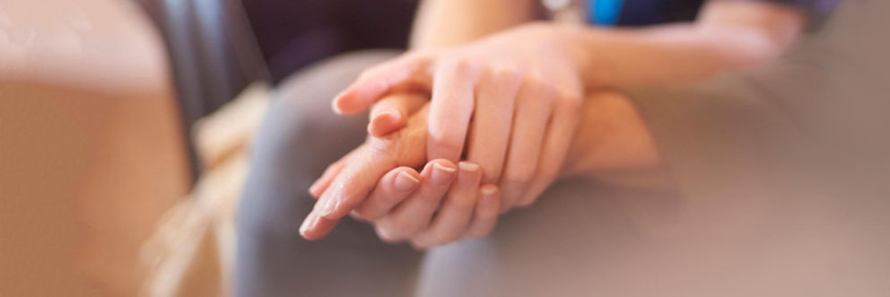 A close-up shot of a woman cradling an older woman's hand in both of hers.