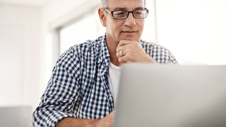 Older man with glasses cupping his chin with his hand and looking at a laptop.