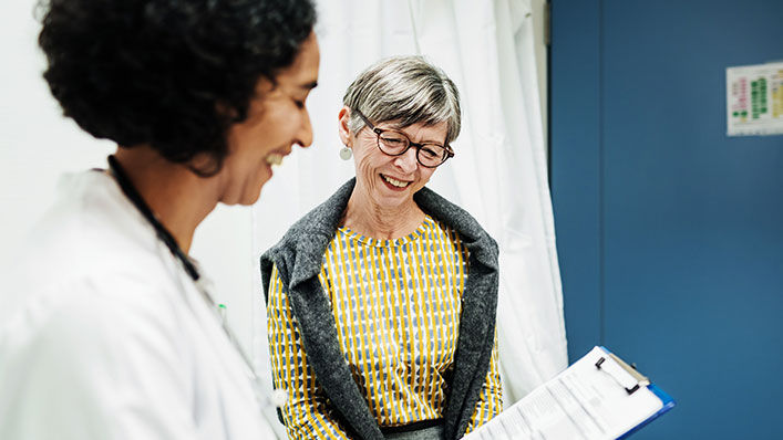 A doctor reviews an intake form with a smiling older patient.