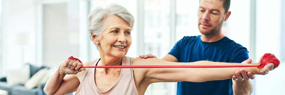 A physical therapist guides an older female patient through an arm exercise.