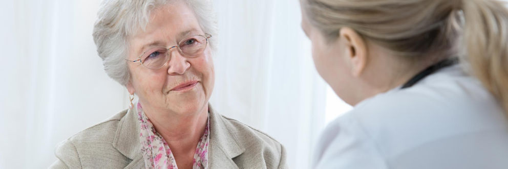 Doctor speaking to older smiling woman in a clinic setting.
