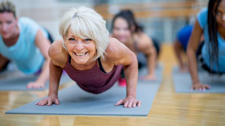 An older woman smiles as she enters a push-up pose in her yoga class.