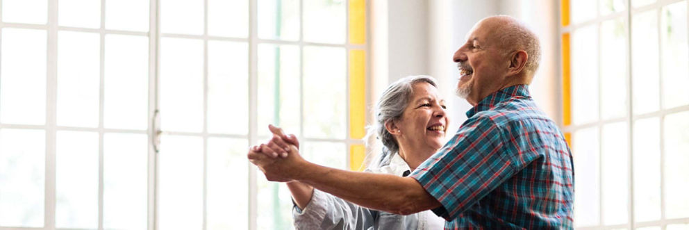 An older man and older woman dance in a sunny room