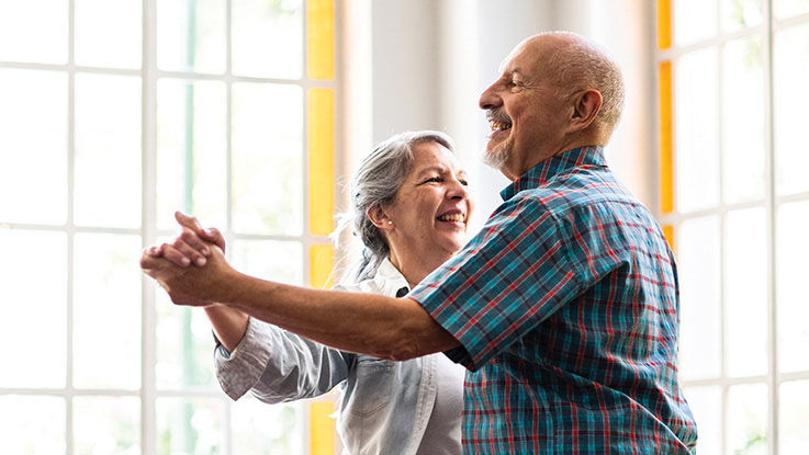 An older man and older woman dance in a sunny room