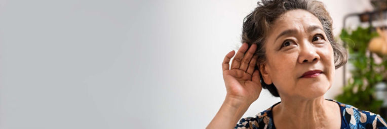 An older woman with age-related hearing loss cups her hand behind her ear and leans close to hear better. 