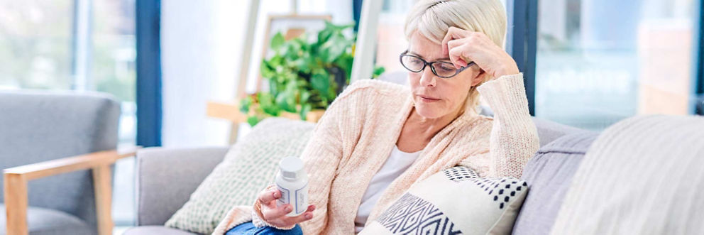 An older woman sitting on a sofa looks at information on a prescription bottle