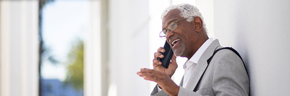 An older man in a gray suit smiles while talking on his cell phone.