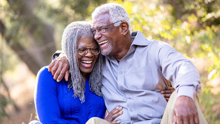 Older man and woman sitting outside with their arms around each other, laughing.