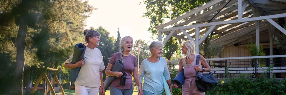 A group of older women laugh and chat while walking to yoga class. 