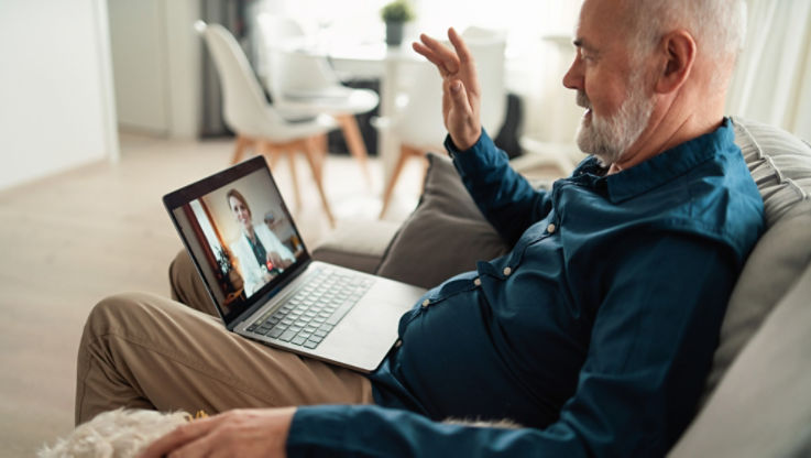 An older man at home speaks with his primary care doctor through his computer during a video visit.