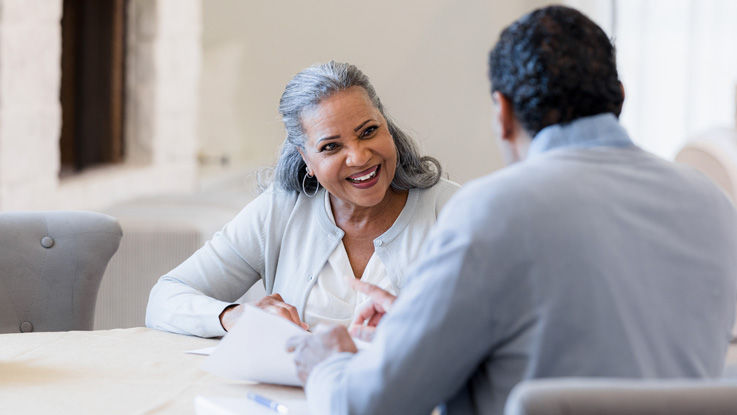 Woman and man sit at a table together, chatting and going over paperwork.
