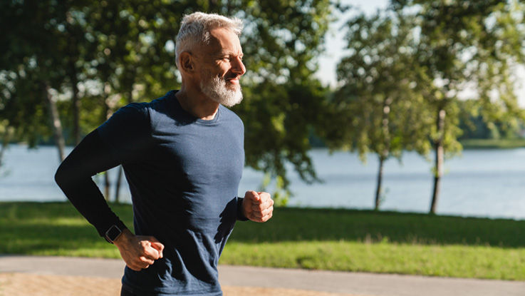 A older man runs on a park path during a sunny summer day.