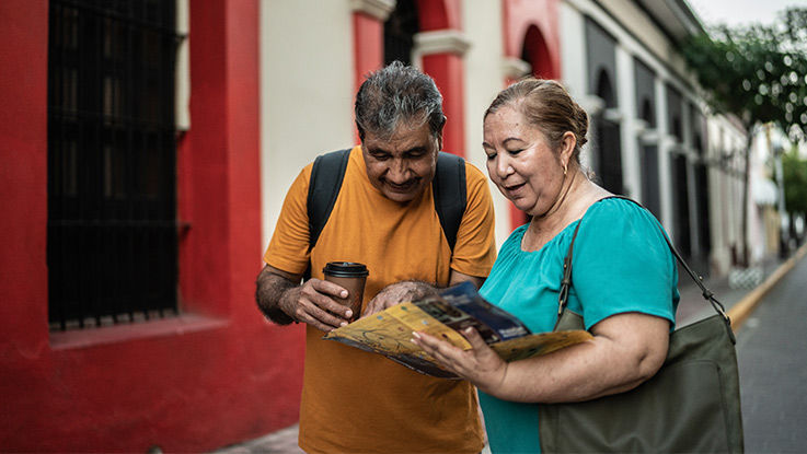 Standing in a city street on vacation, an older husband and wife look at a map.