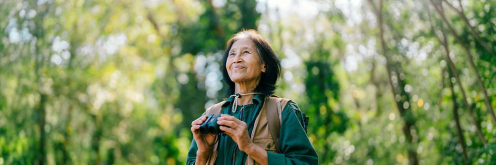 A birdwatcher pauses in the middle of the forest and listens with her binoculars in her hands.