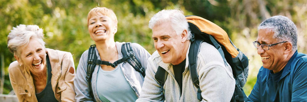 Four older people hiking outside, smiling and laughing.