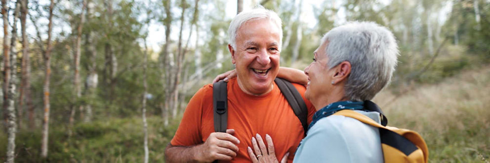 An older man and older woman hike through a scenic forest