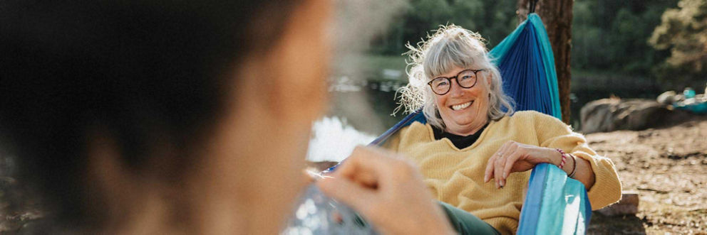 An older woman relaxes in a hammock on a scenic lakeshore