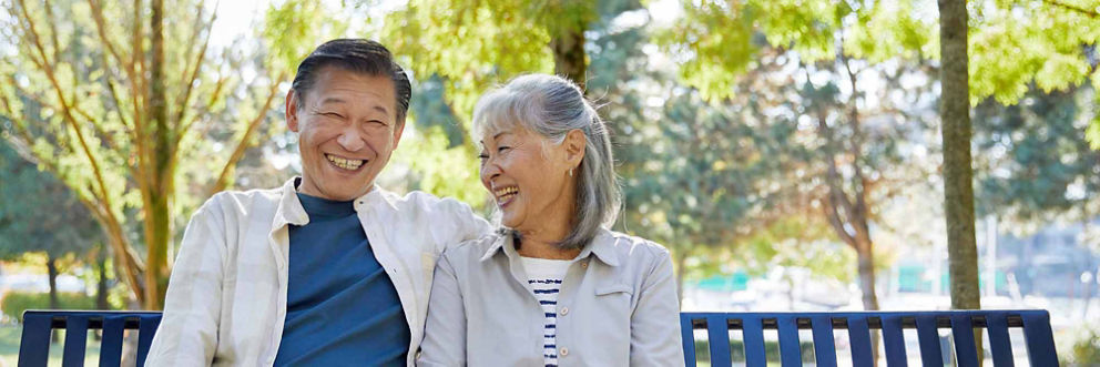 An older couple sits on a park bench, smiling.