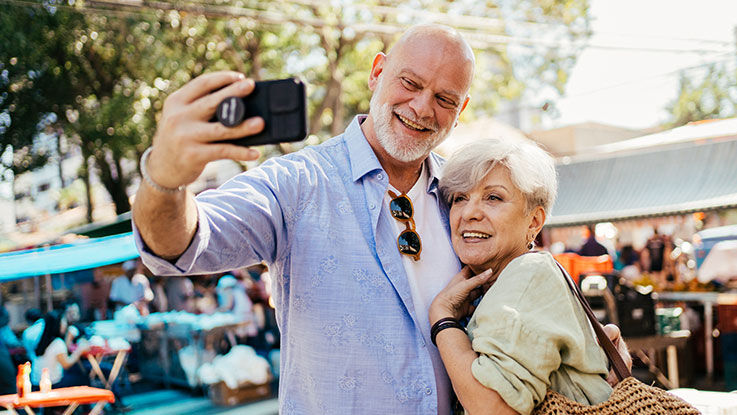 An older couple stand outside and take a selfie.