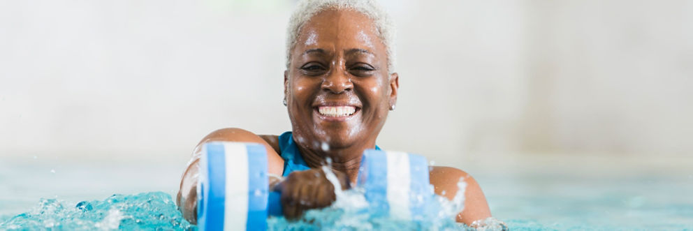 An older woman smiles as she exercises in a pool using an aquatic dumbbell