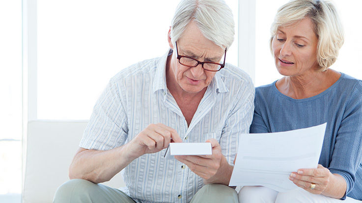 Older man and woman sitting and looking at a calculator in the man's hands and a piece of paper in the woman's hand.