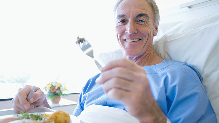 An older man eating from his hospital bed