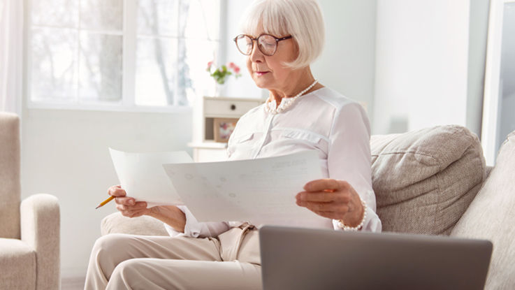 An older woman sits on her couch while reviewing Medicare plan documents.