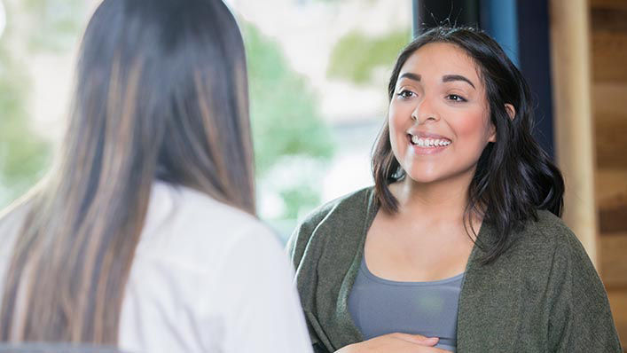 A doctor speaks with a smiling pregnant woman.